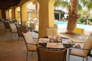 An outdoor dining area with tables set for a meal, surrounded by chairs, and overlooking a pool.