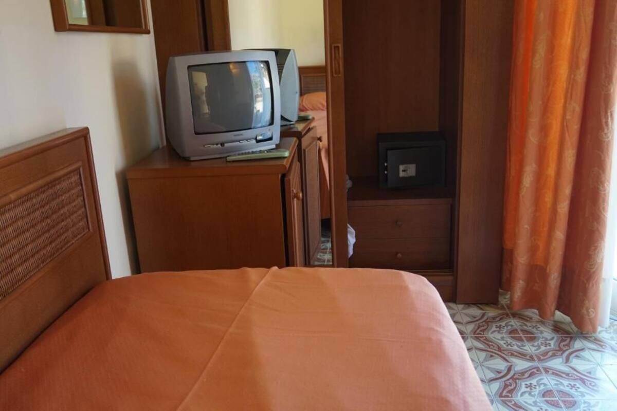 A hotel room with a bed, a wooden nightstand with a television, a dresser, and a wardrobe.