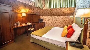 A hotel room with a bed, bedside table, lamp, desk, chair, and a telephone.
