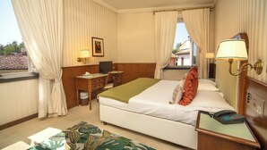 A hotel room with a bed, desk, chair, lamp, and a view of the outside. - Grand Hotel Bastiani (Grosseto)