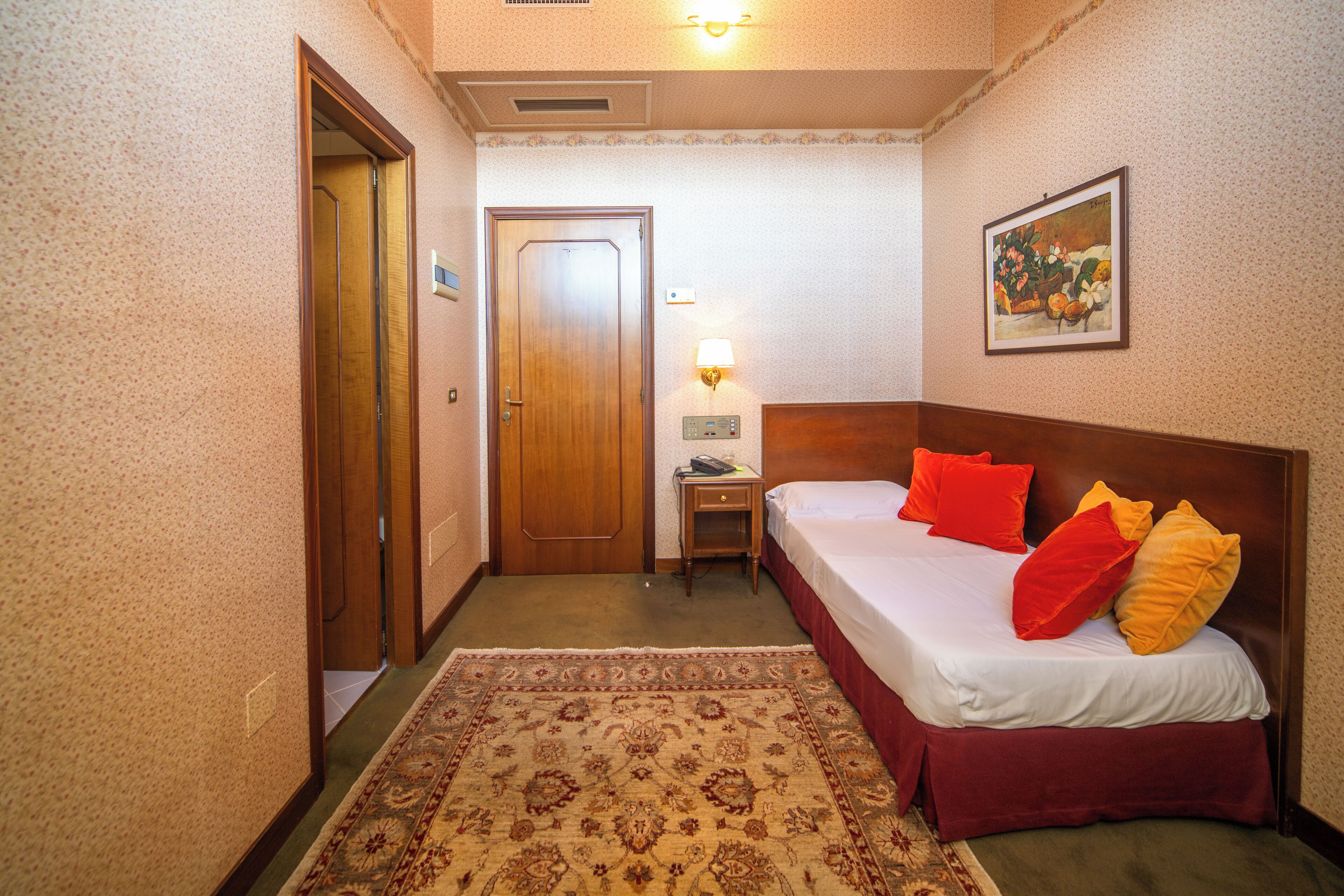 Una habitación de hotel con cama, mesita de noche, lámpara y puerta.