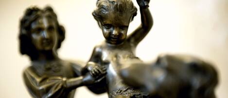 Gros plan d’une sculpture en bronze représentant deux personnages, l’un assis et l’autre debout, sur un fond flou.