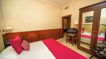 A hotel room with a large bed, a wooden headboard, a desk with a chair, a television, and a wardrobe.