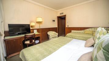A hotel room with two beds, a desk with a television, a chair, and a lamp.
