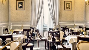 A dining area with tables set for service, framed artwork on the walls, and a large window with curtains. - Grand Hotel Bastiani (Grosseto)
