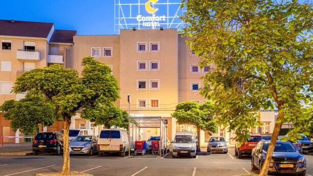 Un Comfort Hotel con vista despejada al estacionamiento, varios autos y árboles al frente.