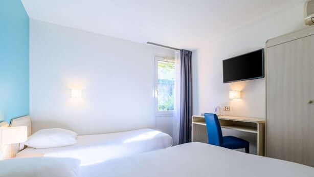 A hotel room with two beds, a desk, a chair, a TV, and a window with curtains. - Comfort Hotel Montlucon (Montlucon)