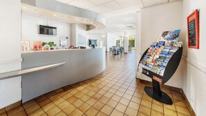 Zona de recepción de un hotel con un mostrador curvo, una máquina de café y una exhibición de folletos.