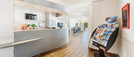 Zona de recepción de un hotel con un mostrador curvo, una máquina de café y una exhibición de folletos.