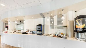 Una barra de desayuno moderna con una máquina de café, estación de té y una vitrina de vidrio.