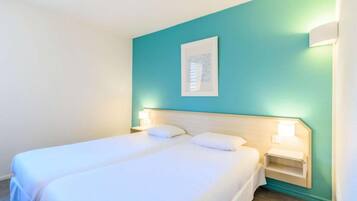 Ein Hotelzimmer mit zwei Betten, türkisfarbenen Wänden und Nachttischlampen.