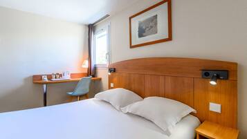 Een hotelkamer met een bed, een bureau, een stoel, een nachtkastje en een lijst aan de muur.