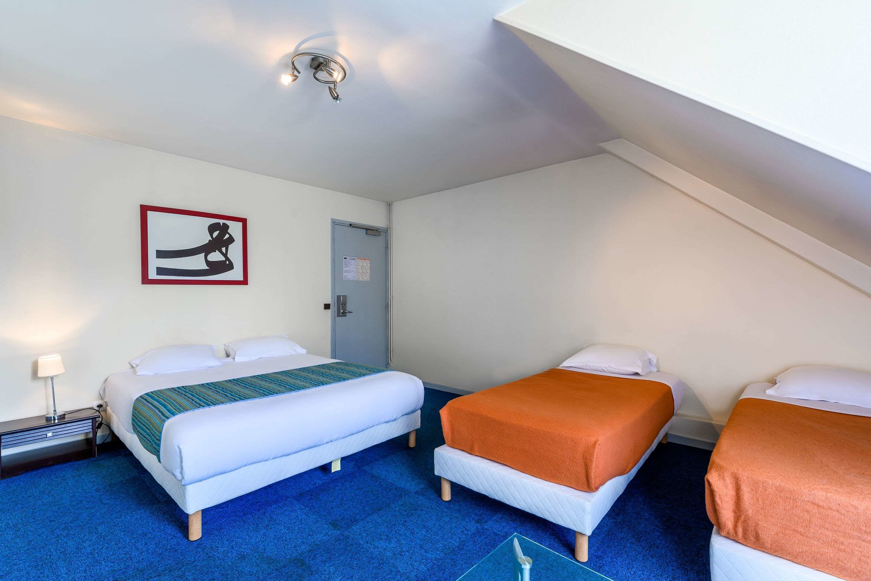 Habitación de hotel con dos camas, alfombra azul, un cuadro enmarcado en la pared y una lámpara en el techo.