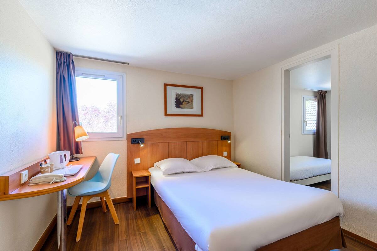 Habitació d'hotel amb un llit, una taula de nit, una cadira, una làmpada i un quadre al mur.