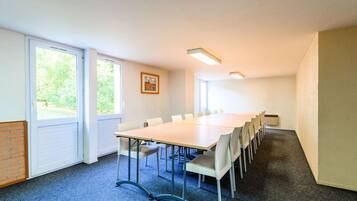 A conference room with a long table, chairs, carpeted floor, windows, and a framed picture on the wall.