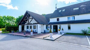 Een gebouw met twee verdiepingen, een schuin dak, een overdekt terras en een parkeerplaats.