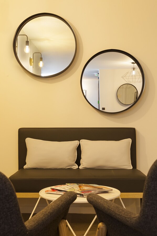 A modern room with a black sofa, two round mirrors, and a small table with magazines.