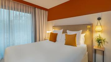 A hotel room with a large bed, a nightstand with a lamp, and a vase with flowers.