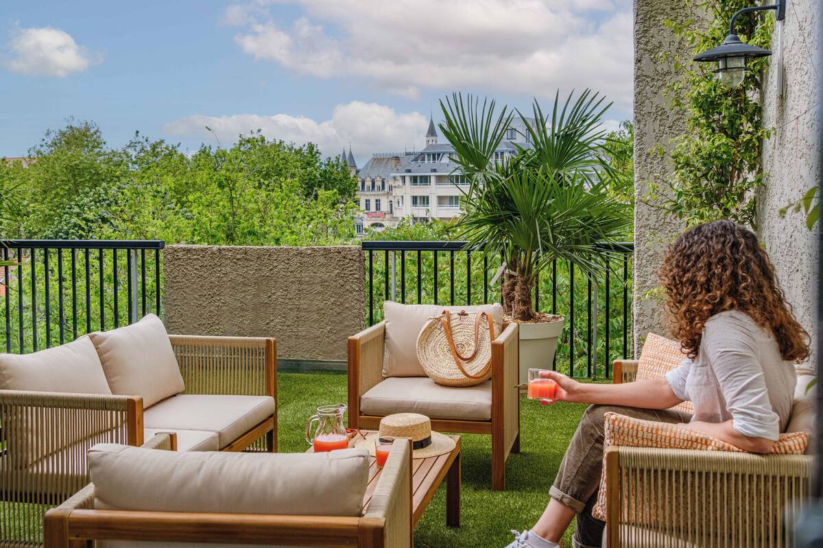 A patio with wicker furniture, a drink, and a view of a building in the background.