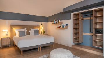 Un dormitorio moderno con una cama, mesitas de noche, un zapatero, un otoman redondos y un armario, además de una estantería de pared con libros.