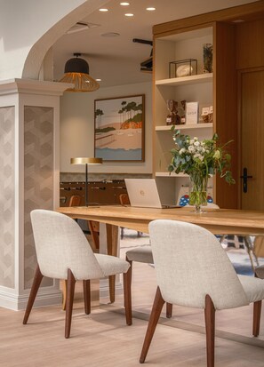 A modern dining area with a wooden table, two upholstered chairs, a laptop, and a vase with flowers. - Arcanse by Inwood Hotels (Arcachon)