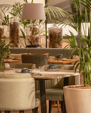 A cozy indoor seating area with tables and chairs, surrounded by potted plants and decorative vases. - Arcanse by Inwood Hotels (Arcachon)