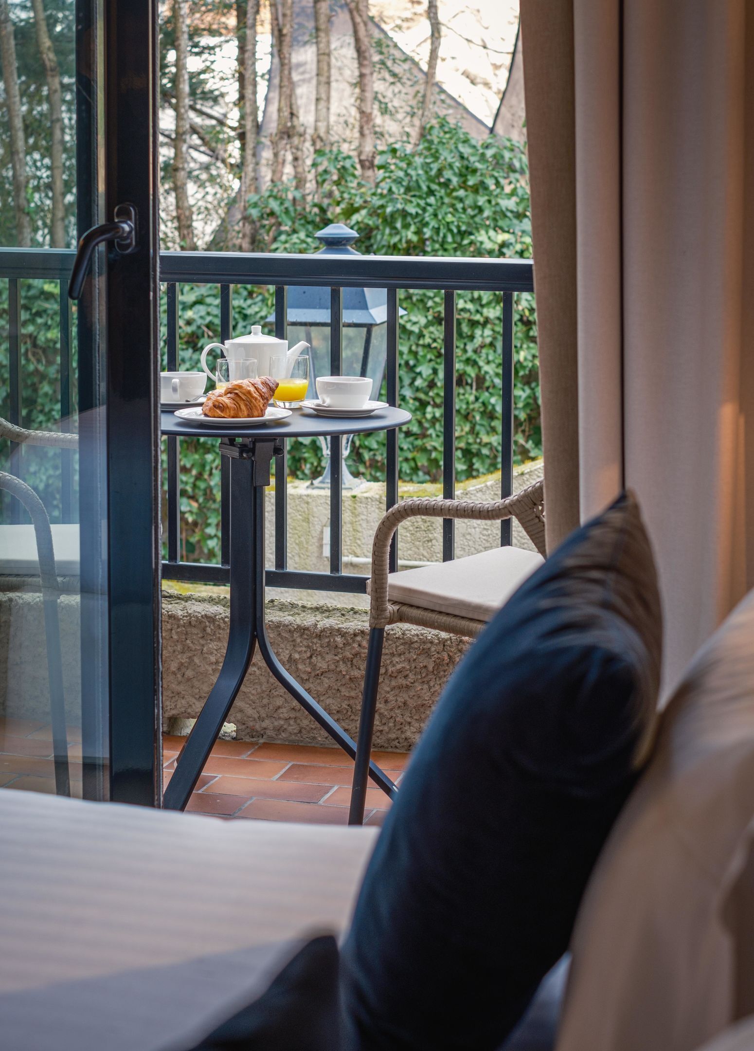 Un balcón con una mesa dispuesta para el desayuno, que incluye croissants, zumo de naranja y café.