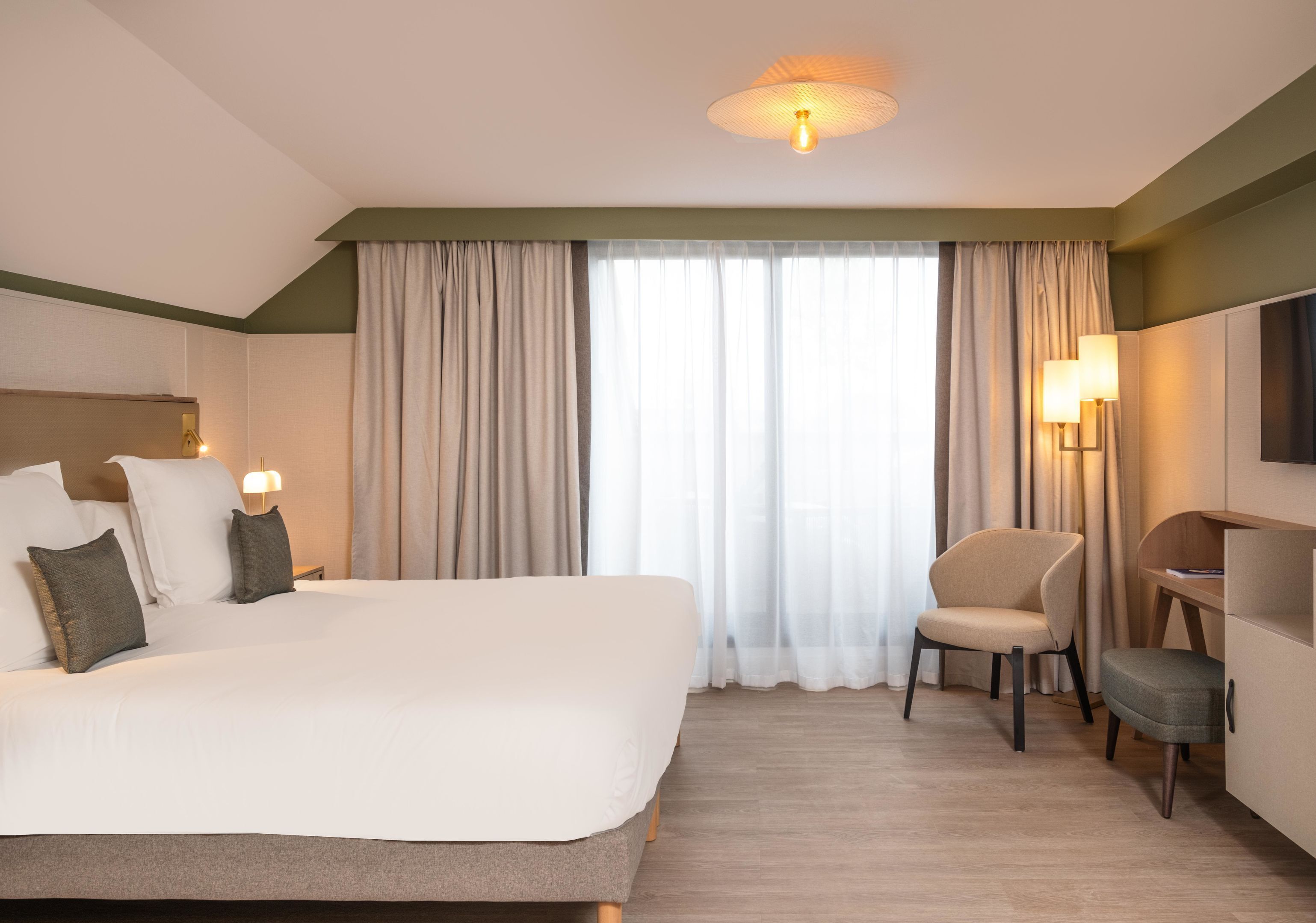 A hotel room with a large bed, a chair, a desk, and a television.