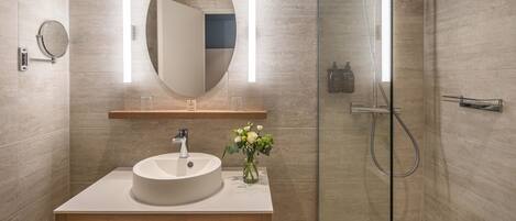 A modern bathroom with a round sink, a mirror, and a shower.