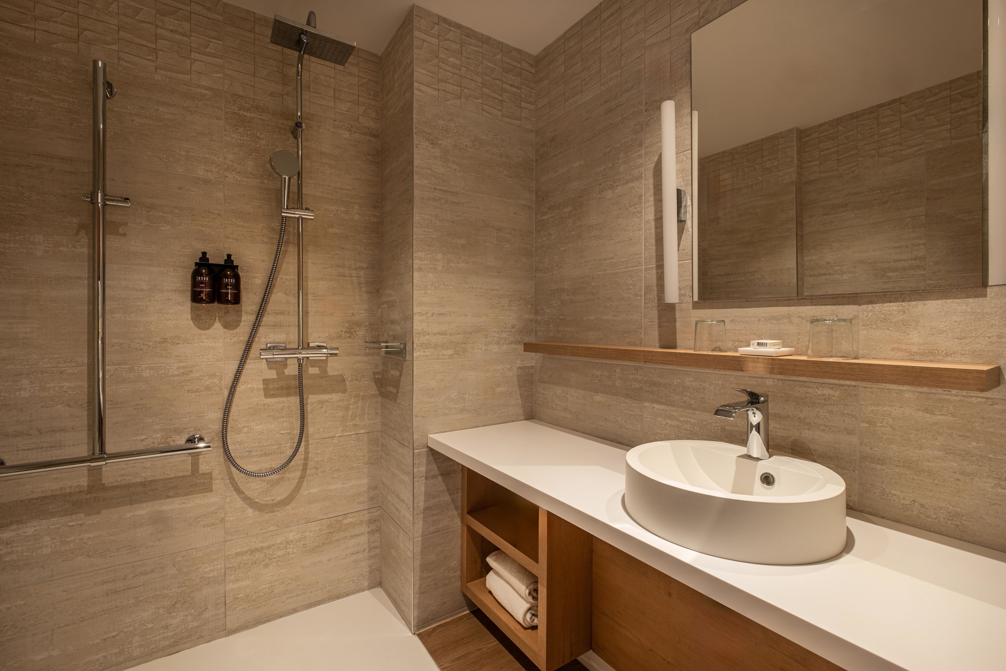 Ein modernes Badezimmer mit bodengleicher Dusche, großem Spiegel und rundem Waschbecken.