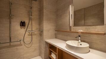 Un baño moderno con ducha a ras de suelo, un espejo grande y un lavabo redondo.
