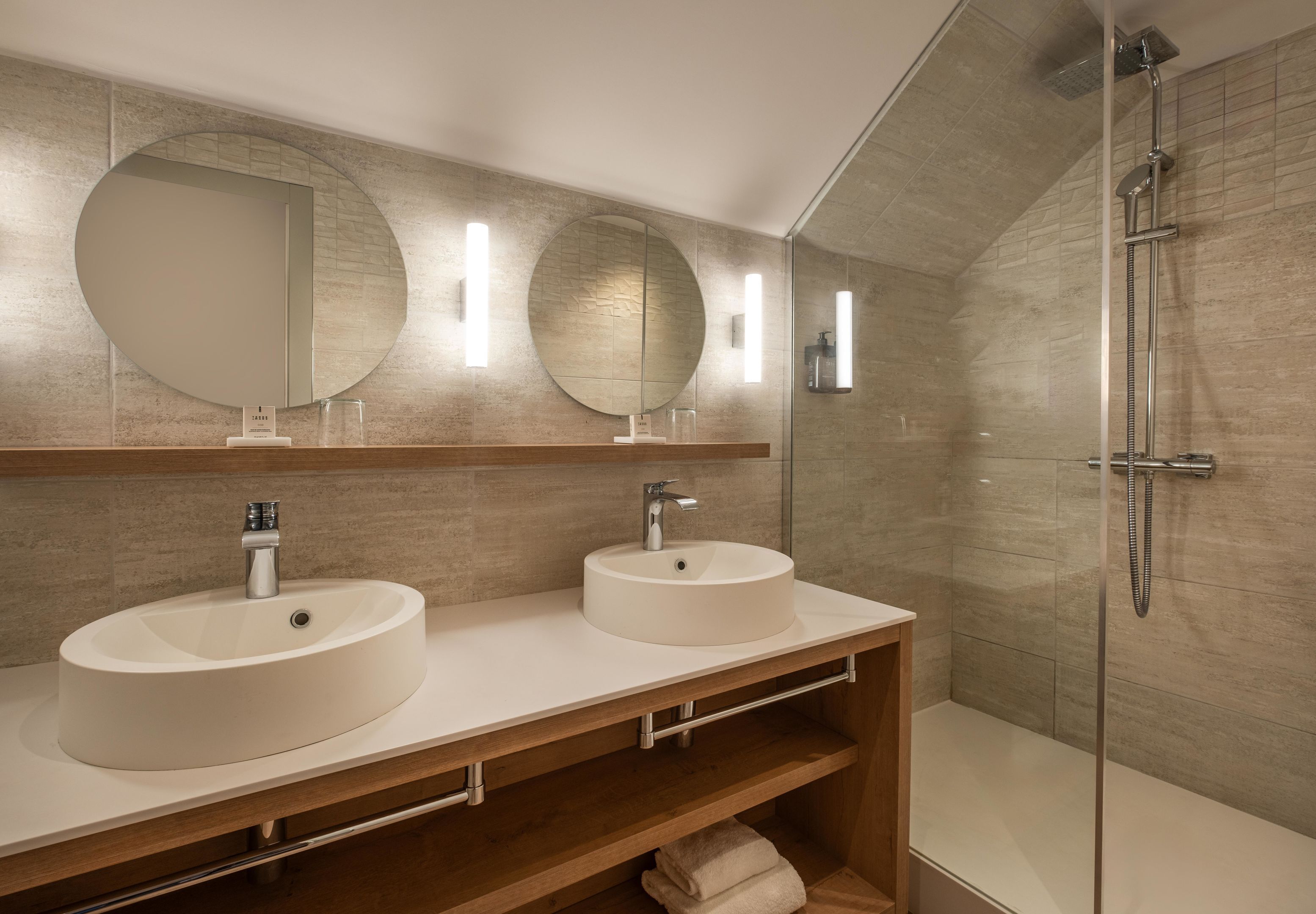 A modern bathroom with two sinks, a large mirror, and a glass-enclosed shower.