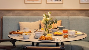 Un comedor con una mesa redonda dispuesta para el desayuno, un sofá y cuadros en la pared.