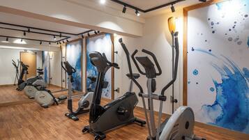 A gym with multiple stationary bikes and cardio machines, wooden flooring, and a large mirror on the wall.