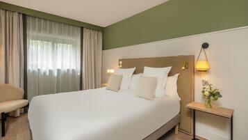 Ein Hotelzimmer mit einem großen Bett, einem Nachttisch mit Lampe, einem Sessel und einem Fenster mit Vorhängen.