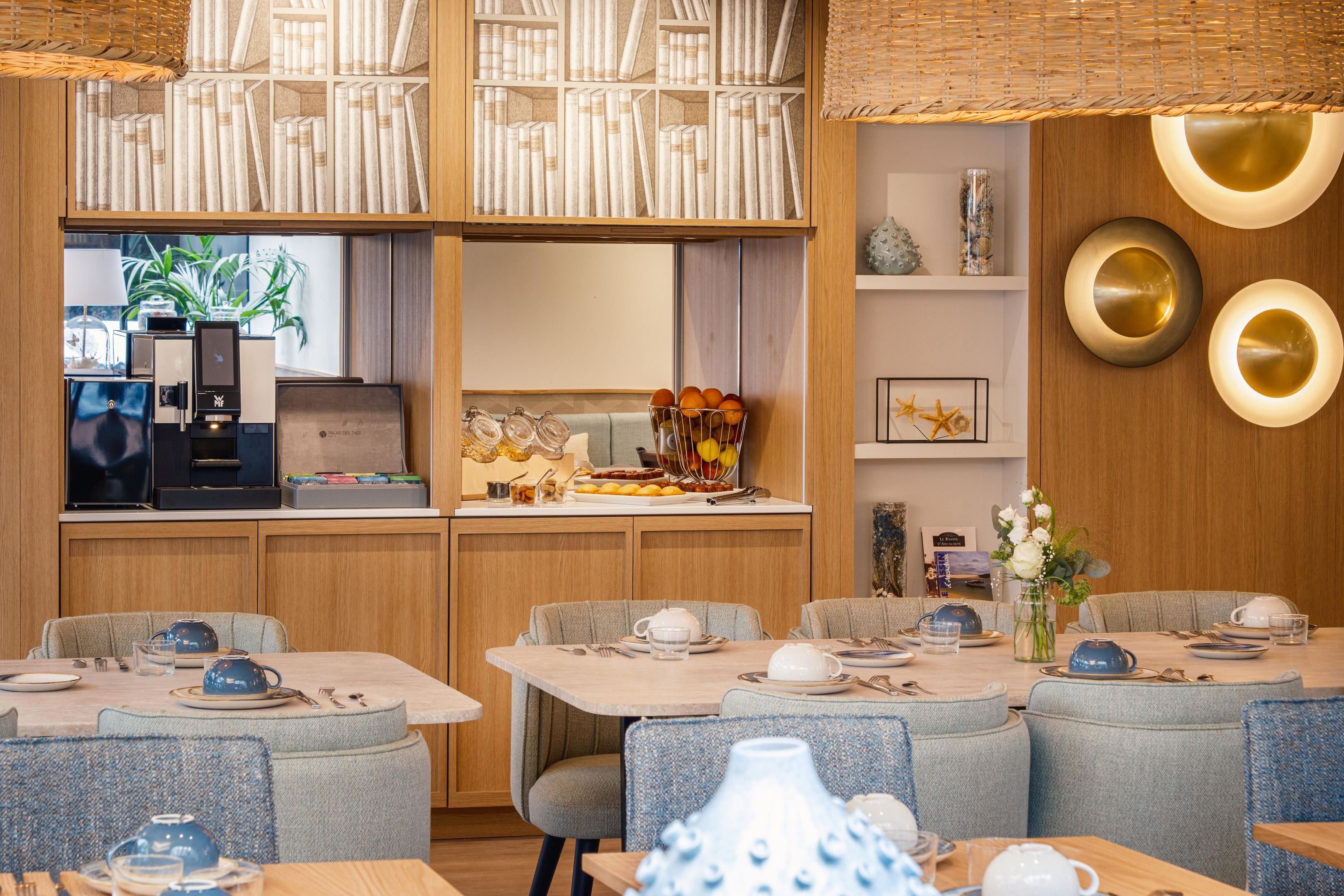 Un restaurant doté de plusieurs tables, d’un appareil à café et d’une bibliothèque remplie de livres.