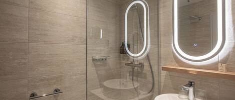 Un bagno moderno con doccia vetrata, uno specchio rotondo illuminato a LED e un lavandino bianco con ripiano in legno sopra.