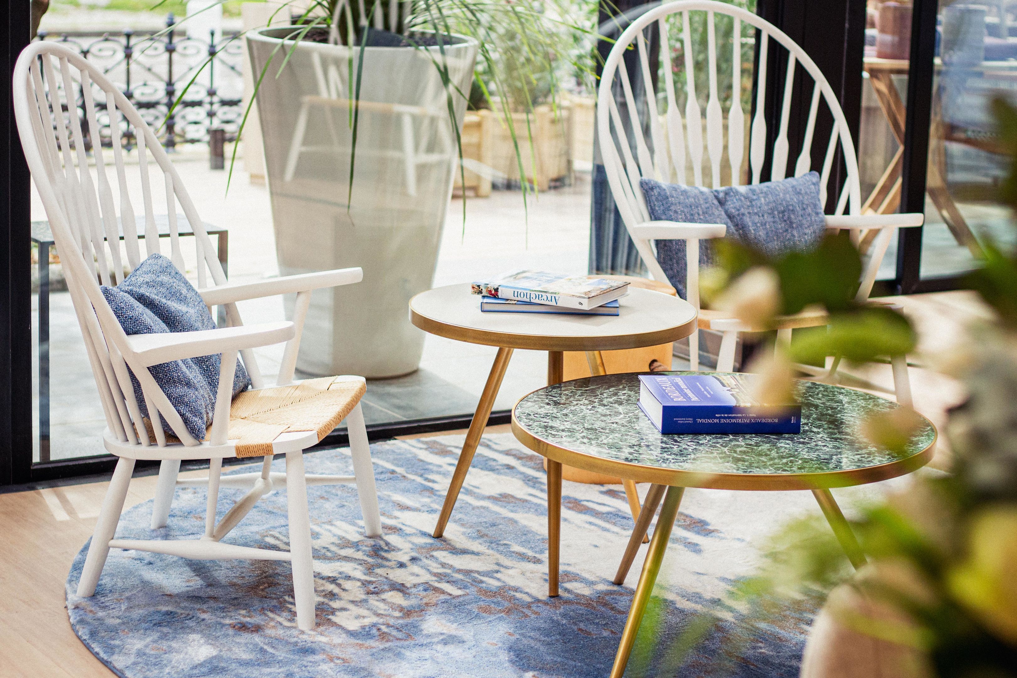 A seating area with two white chairs, a small round table, and a large potted plant.