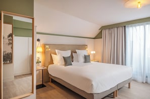 A hotel room with a large bed, bedside lamps, a nightstand, a mirror, and a window with curtains.