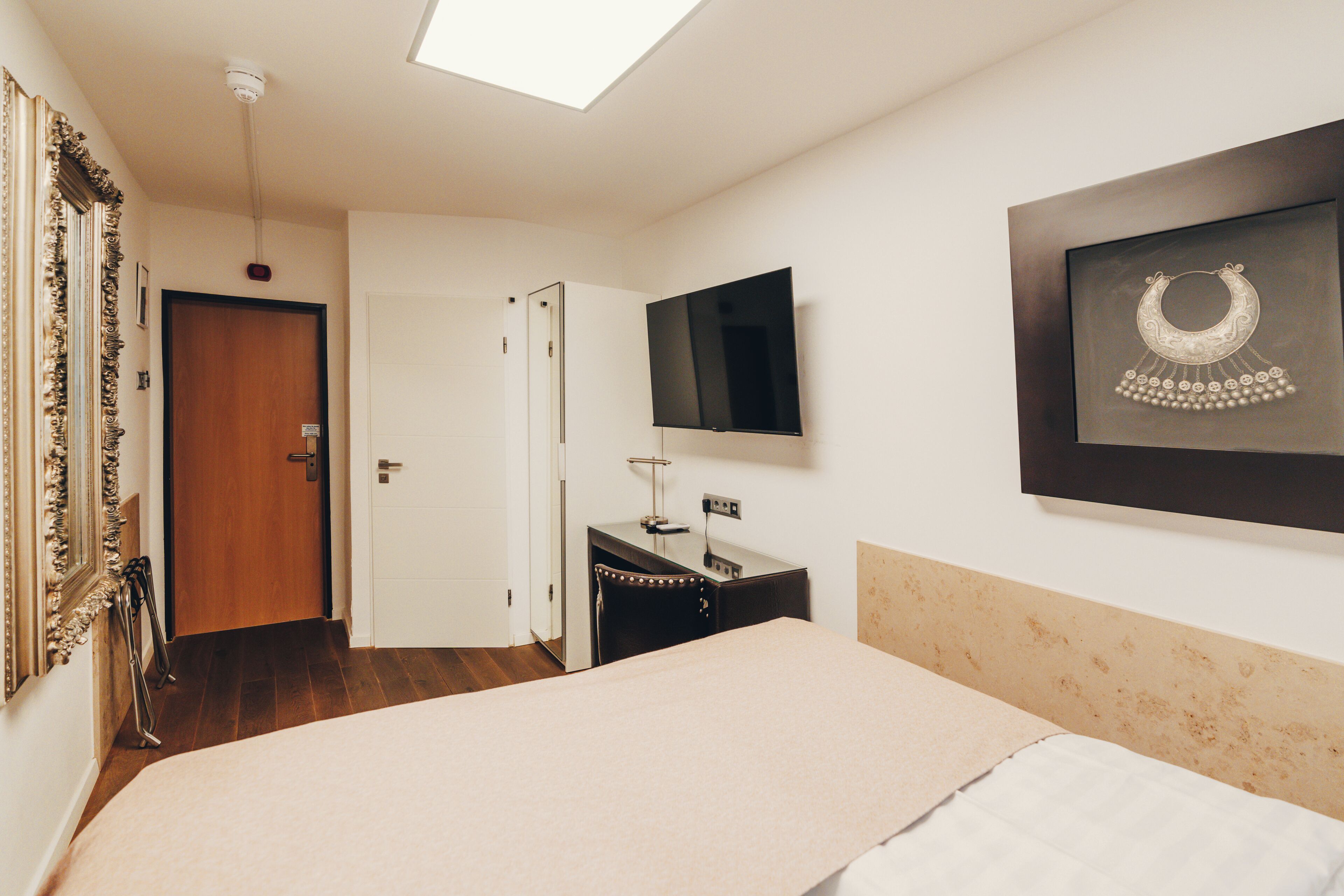 A bedroom with a bed, a desk, a chair, a TV, and a framed picture on the wall.