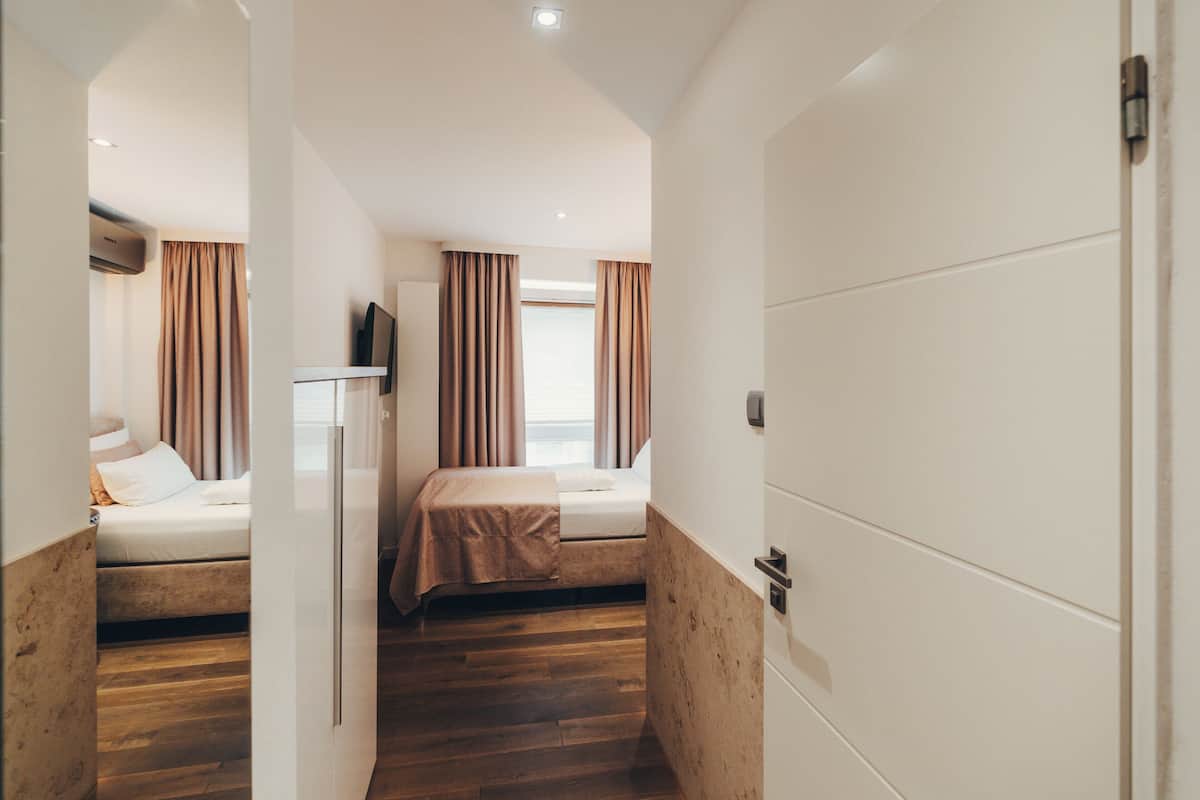A hotel room with two beds, wooden flooring, a white wardrobe, and a flat-screen TV.