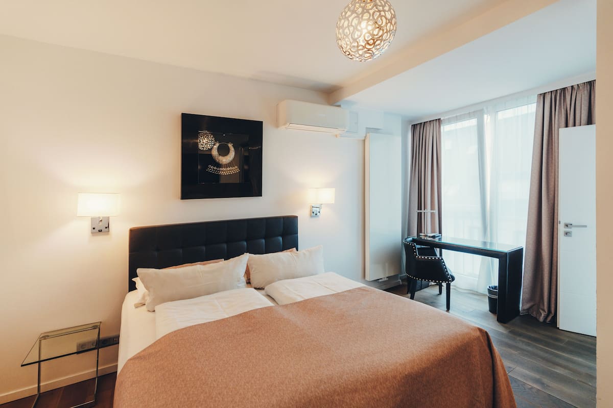 A hotel room with a large bed, a desk, and a window with curtains.