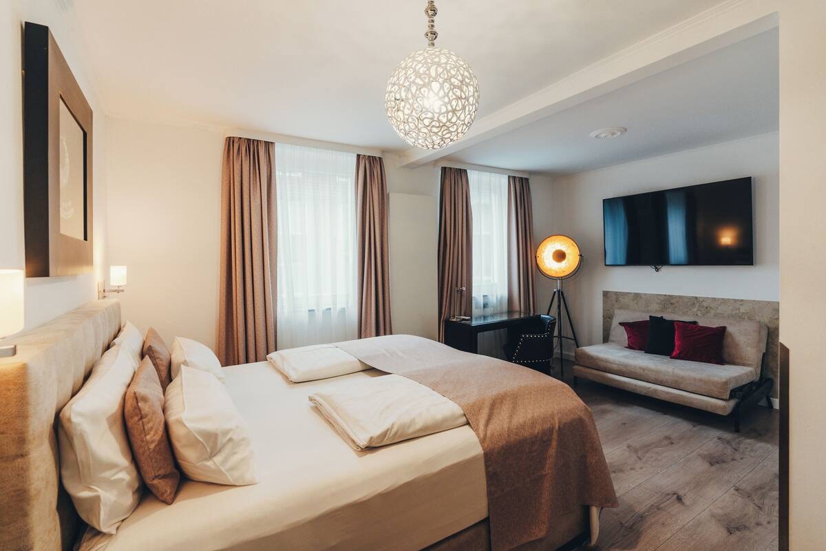 A hotel room with a bed, a sofa, a desk, a lamp, and a TV.