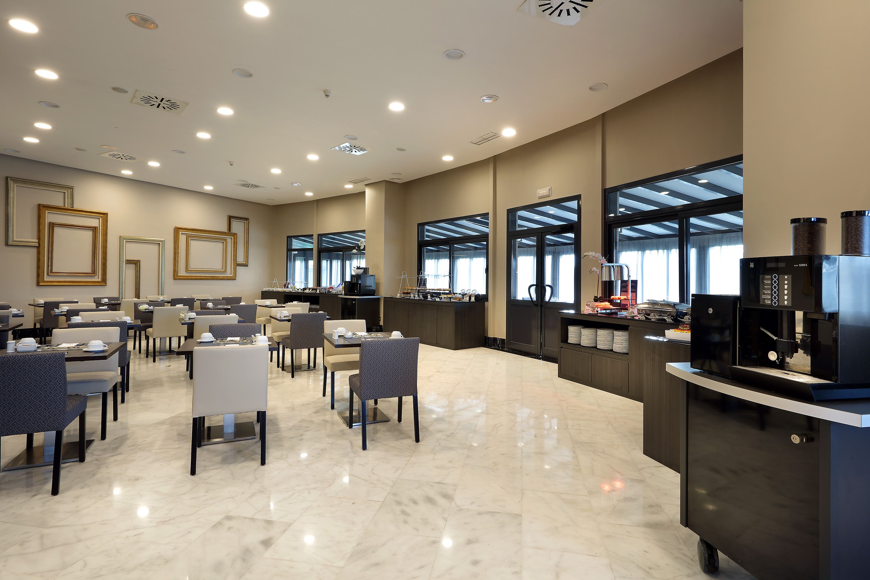 Un vestíbulo de hotel moderno con un amplio espacio de descanso, una recepción y grandes ventanales que permiten la entrada de luz natural.