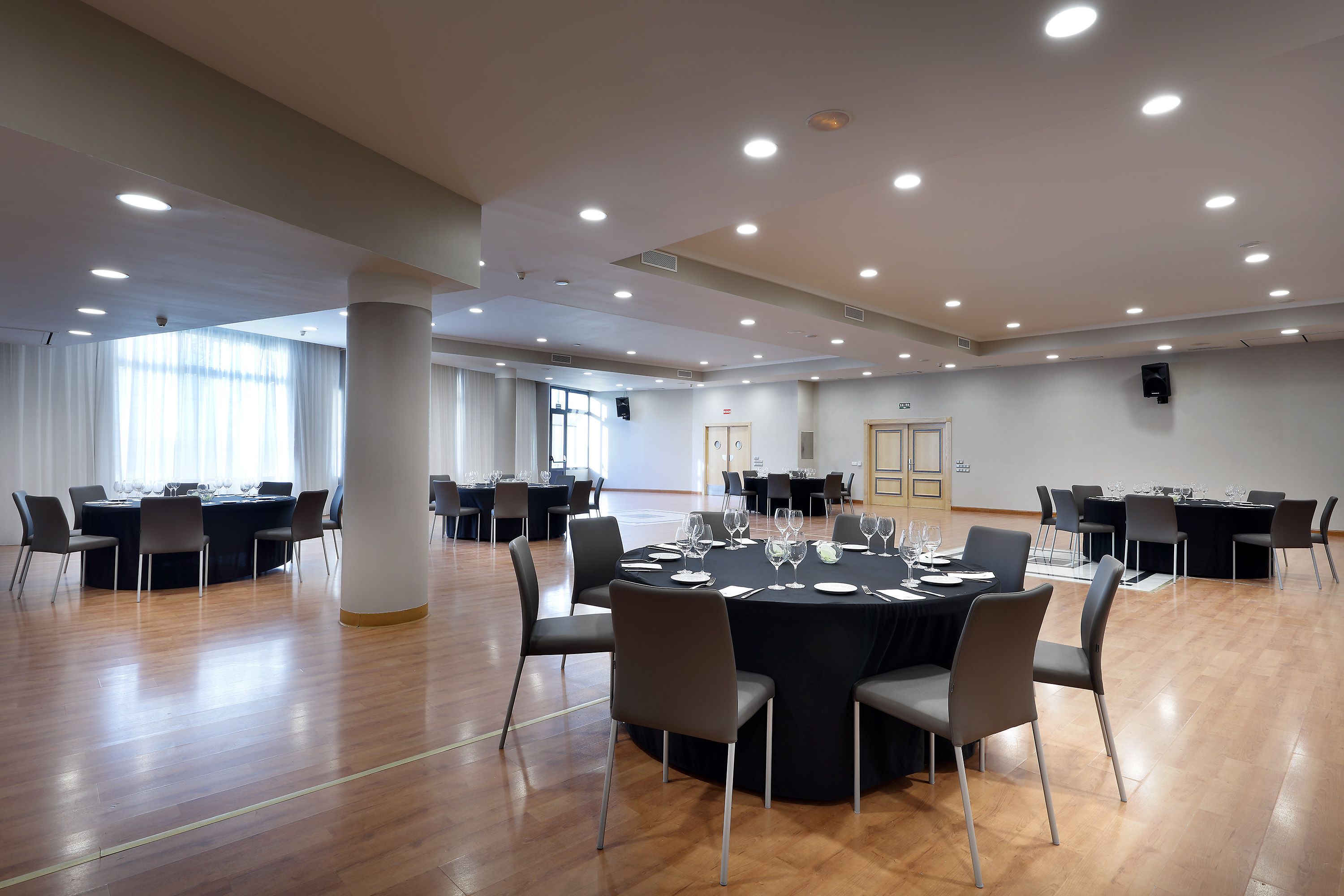 Una amplia sala de conferencias con varias mesas y sillas, ventanas grandes y un techo alto con iluminación empotrada.