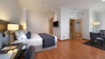 A hotel room with a bed, bedside table, lamp, TV, and a desk with a chair.