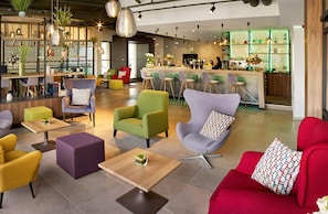 Un hall d’hôtel moderne doté d’un bar, d’espaces aménagés avec des sièges et de plantes décoratives.