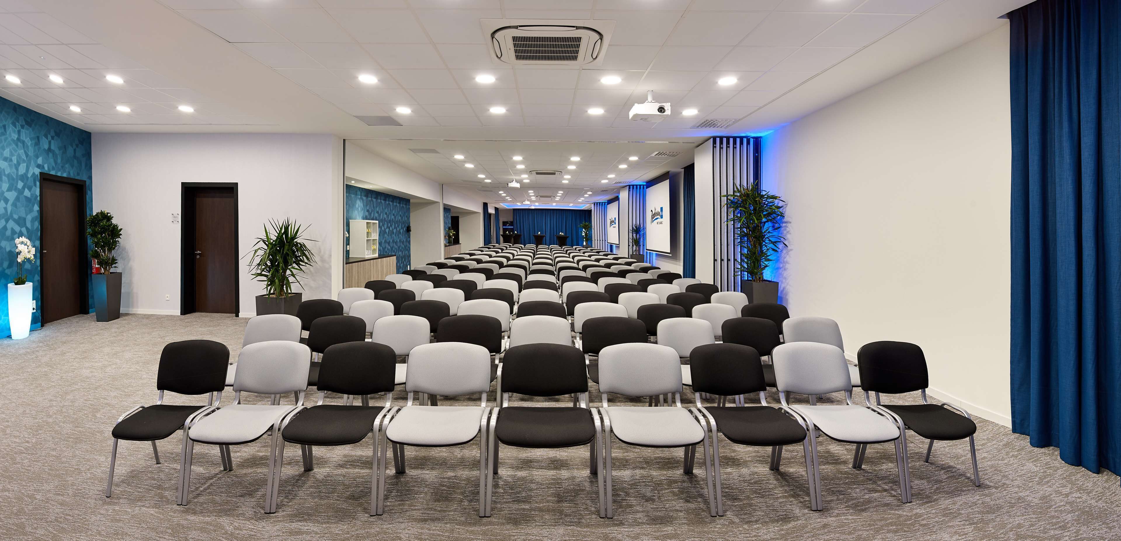 A conference room with rows of chairs, a projector, and a blue curtain.