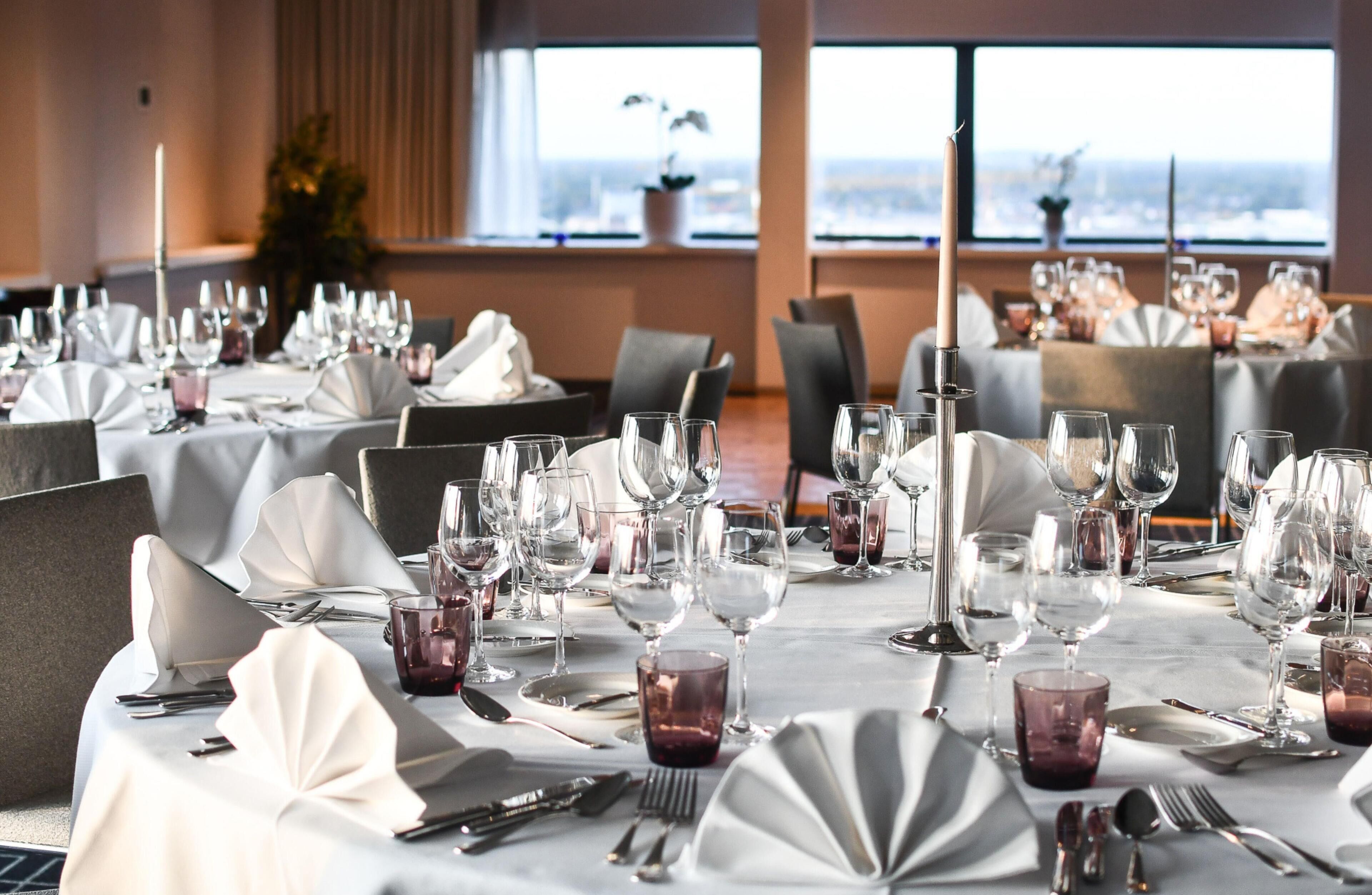 A dining area with multiple tables set for a meal, featuring white tablecloths, silverware, and wine glasses.