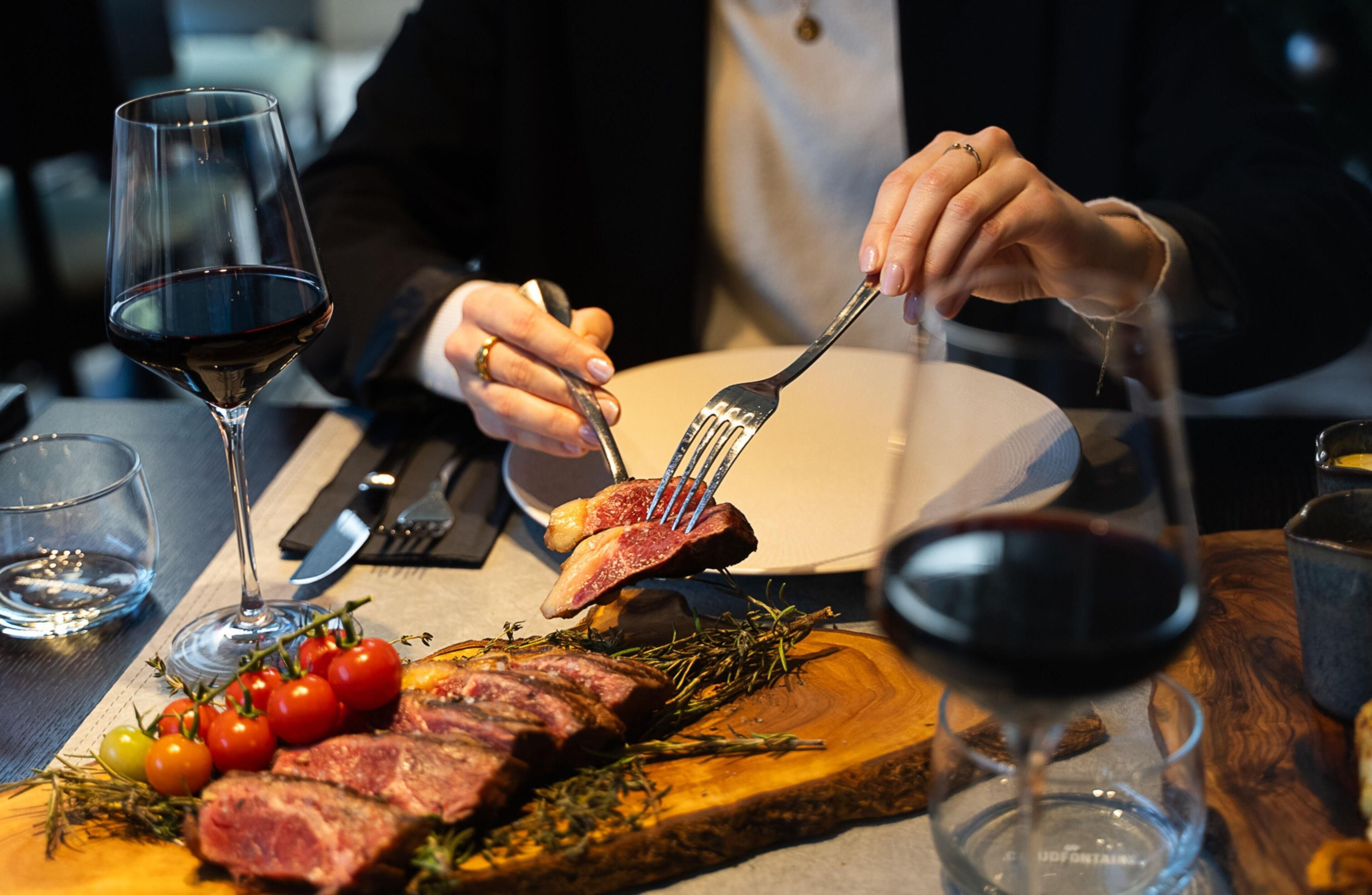 A dining table with a steak, tomatoes, and a glass of red wine.